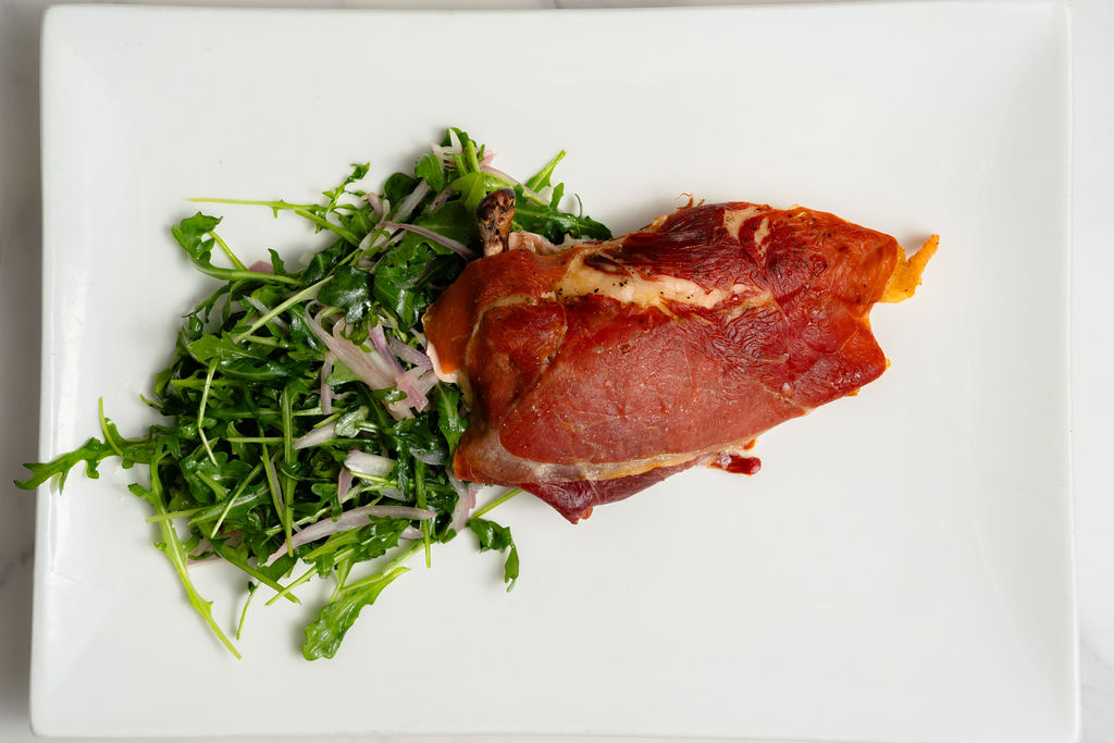 rocket salad plated with purple onions and prosciutto on a white square plate